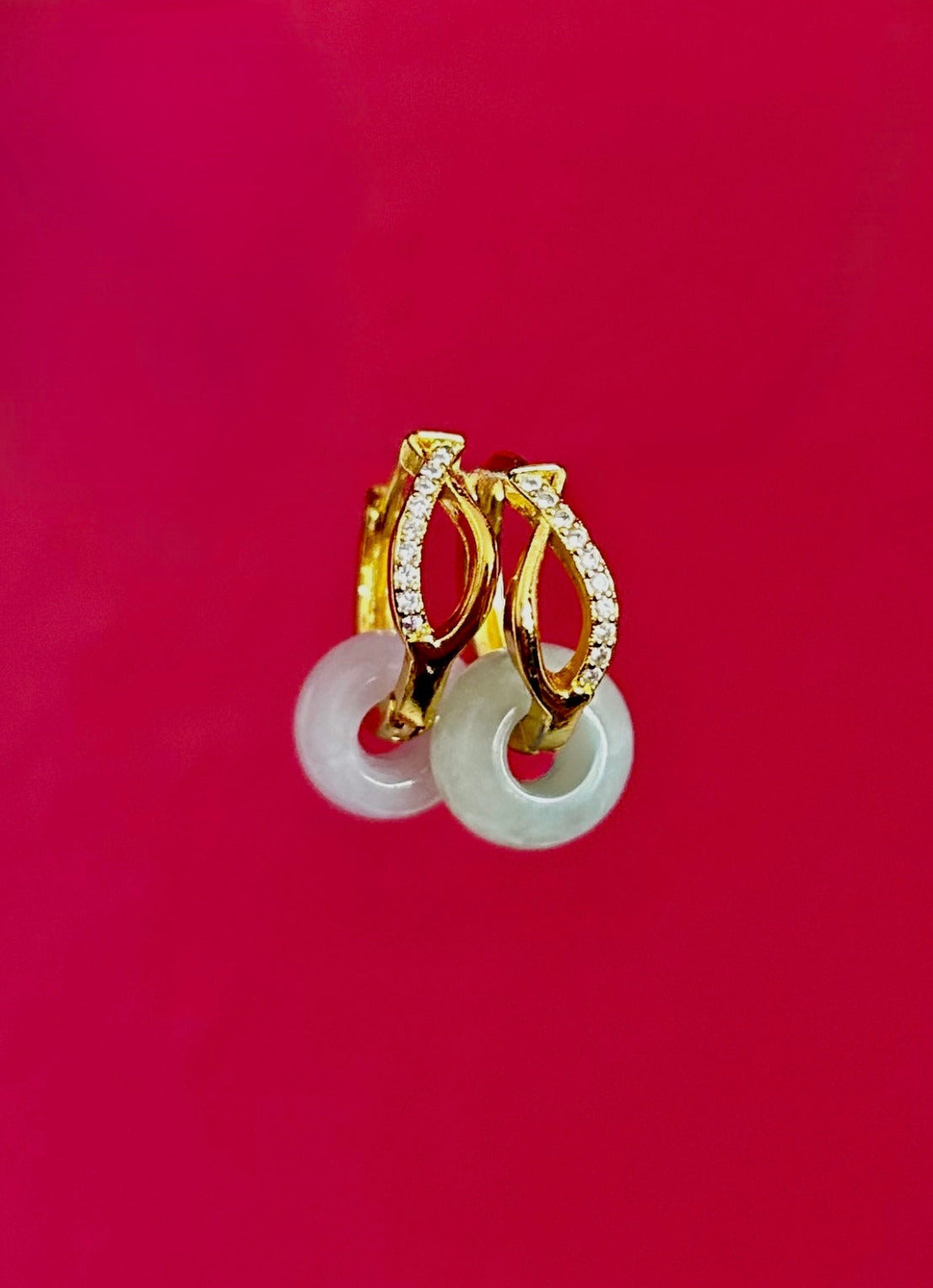 Gold hoop earrings with white jadeite stones on a red background